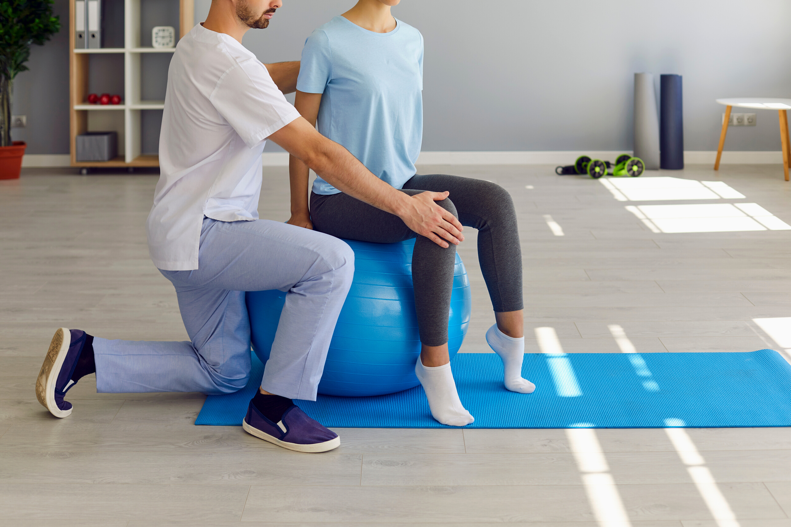 Young Woman Doing Back Fitness Exercise on Fitball with Physiotherapist or Chiropractor Helping Her